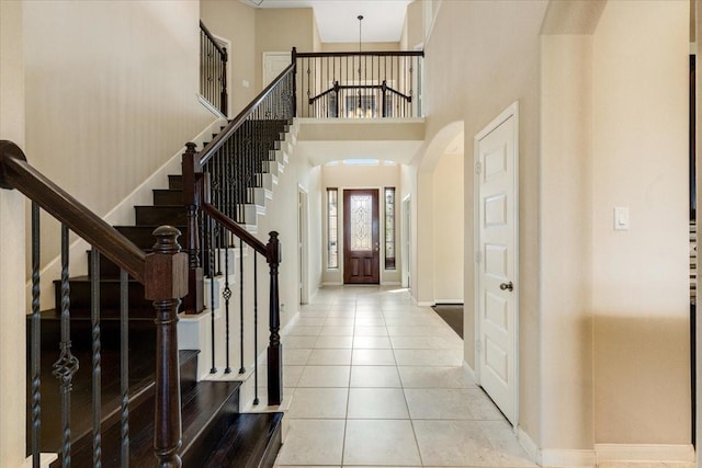 entrance foyer with arched walkways, baseboards, light tile patterned flooring, and a high ceiling