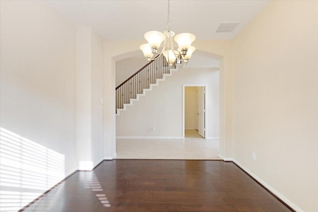 spare room with arched walkways, a notable chandelier, wood finished floors, visible vents, and baseboards