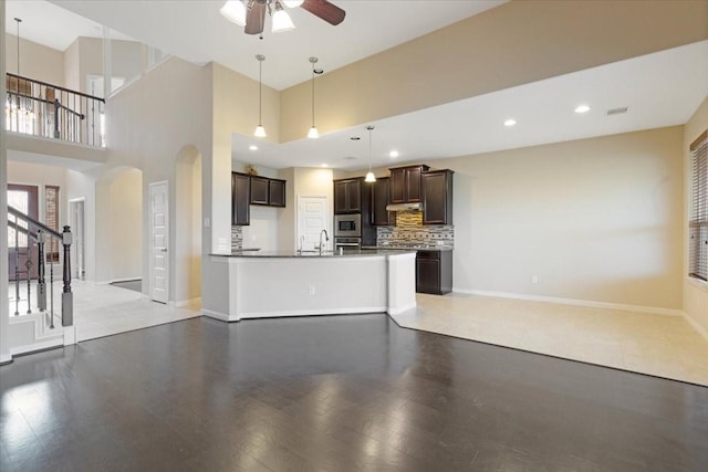 unfurnished living room with arched walkways, recessed lighting, a ceiling fan, baseboards, and stairs