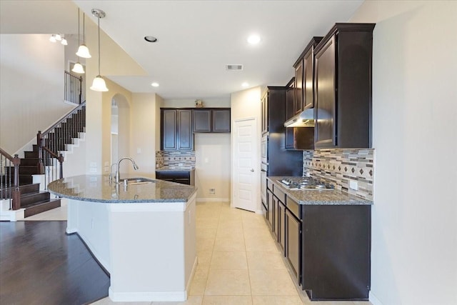 kitchen with dark brown cabinetry, visible vents, dark stone counters, decorative light fixtures, and a sink