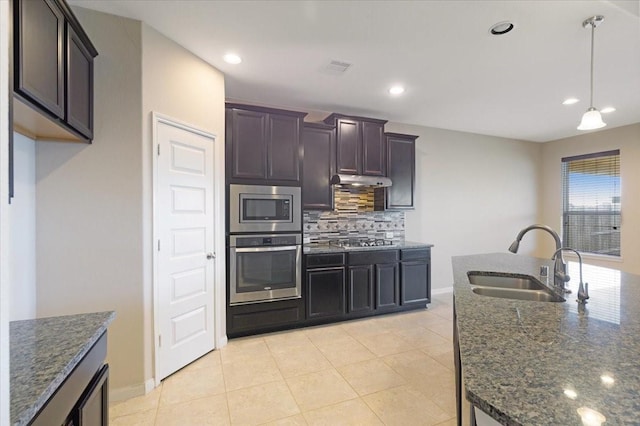 kitchen featuring dark brown cabinetry, stainless steel appliances, a sink, backsplash, and dark stone countertops