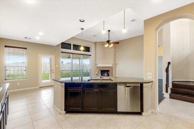 kitchen with hanging light fixtures, stainless steel dishwasher, open floor plan, a sink, and dark stone counters