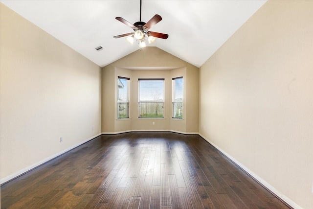 spare room featuring dark wood-style flooring, visible vents, a ceiling fan, vaulted ceiling, and baseboards