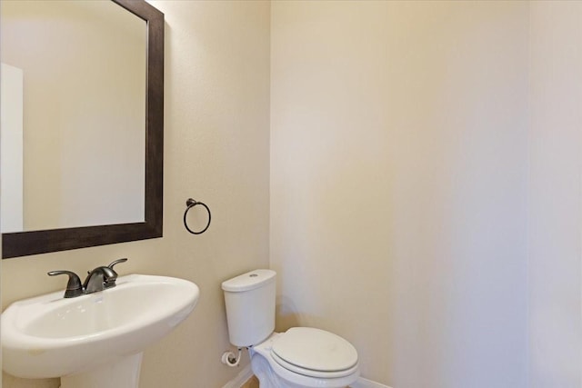 half bath featuring toilet, baseboards, and a sink