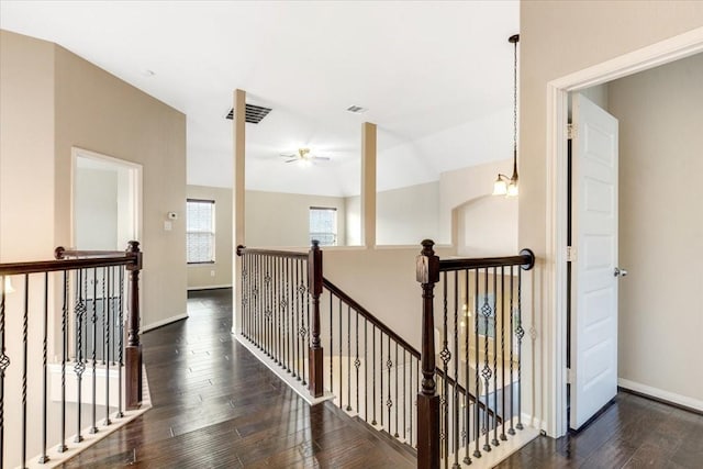 corridor featuring baseboards, visible vents, dark wood finished floors, and an upstairs landing