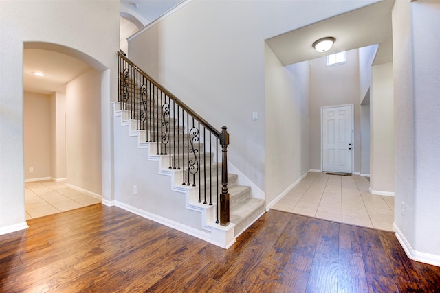 foyer featuring arched walkways, a high ceiling, baseboards, stairway, and wood-type flooring