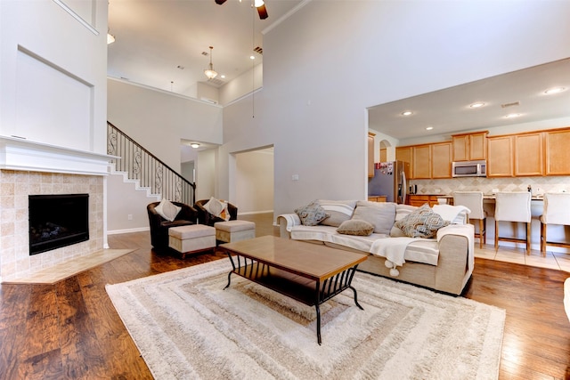 living area with a fireplace, a high ceiling, a ceiling fan, wood finished floors, and baseboards