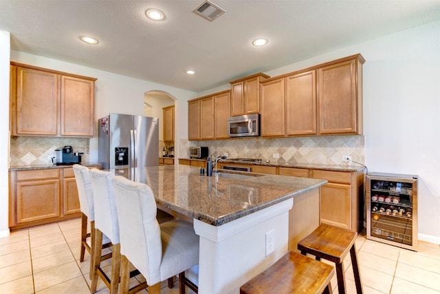 kitchen with arched walkways, wine cooler, visible vents, a kitchen breakfast bar, and appliances with stainless steel finishes