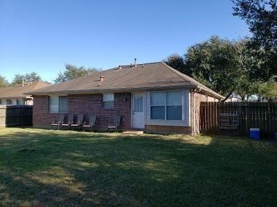 rear view of house with a fenced backyard, a yard, and brick siding