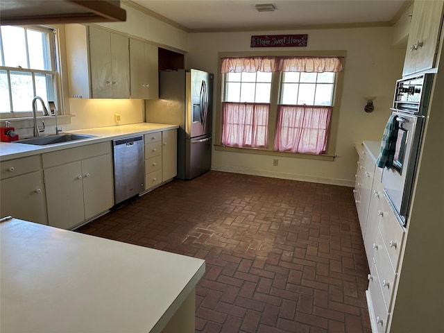 kitchen with a sink, stainless steel appliances, ornamental molding, and light countertops