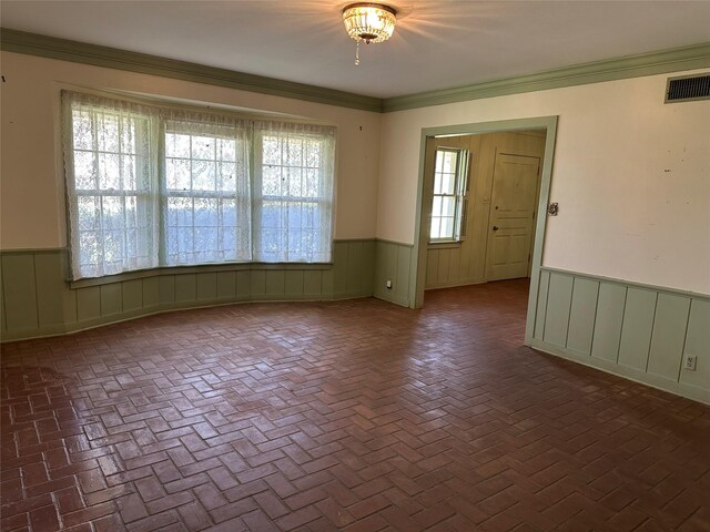 spare room featuring visible vents, wainscoting, brick floor, and ornamental molding