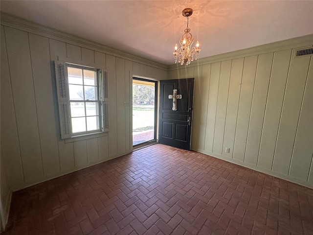 foyer entrance with visible vents, brick floor, crown molding, a decorative wall, and a notable chandelier