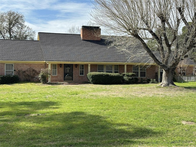 view of front of home with brick siding, a chimney, a front yard, and roof with shingles