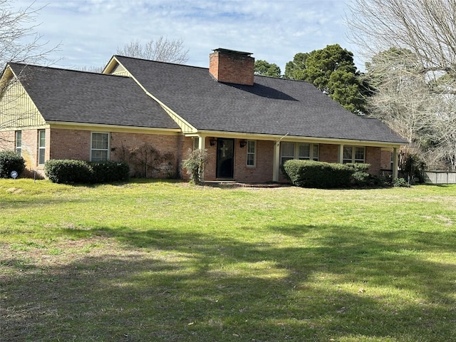 view of front of house with a shingled roof, a front yard, brick siding, and a chimney