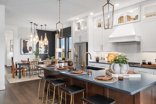 kitchen featuring premium range hood, white cabinets, dark countertops, a kitchen bar, and glass insert cabinets