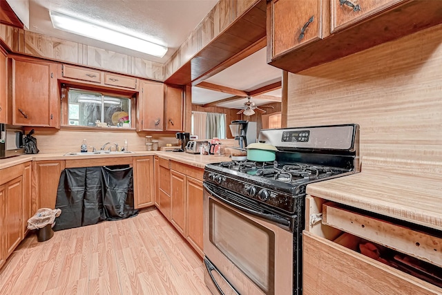 kitchen featuring a sink, light countertops, light wood finished floors, brown cabinetry, and gas stove