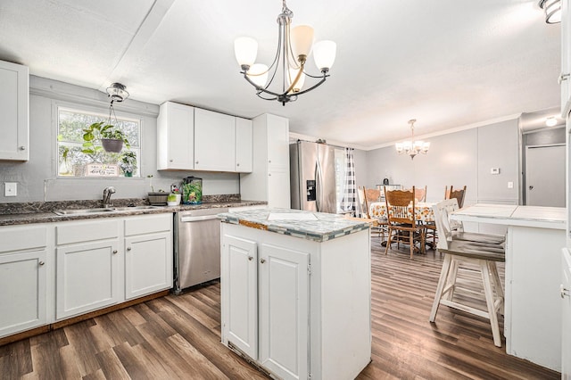 kitchen with pendant lighting, appliances with stainless steel finishes, white cabinetry, a kitchen island, and a chandelier