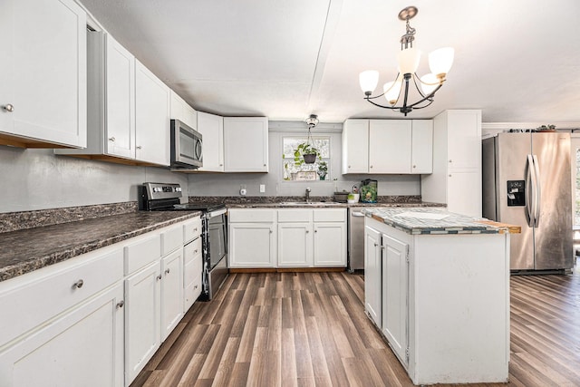 kitchen featuring stainless steel appliances, white cabinetry, hanging light fixtures, and a sink