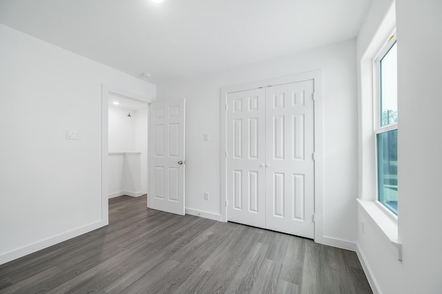 unfurnished bedroom featuring dark wood-style floors, a closet, and baseboards