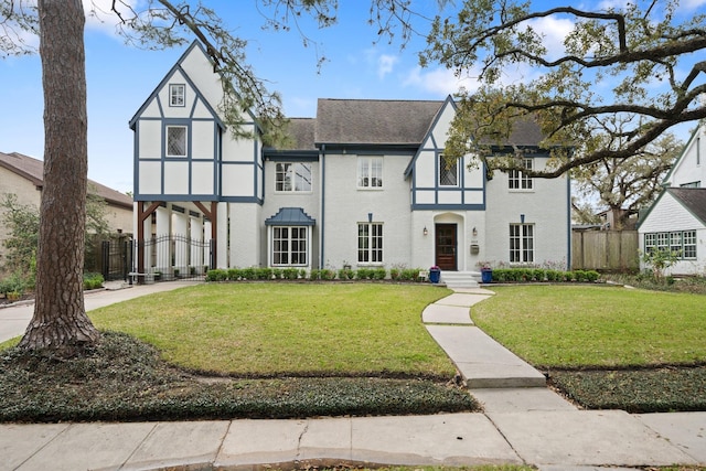 english style home featuring brick siding, a front lawn, and fence