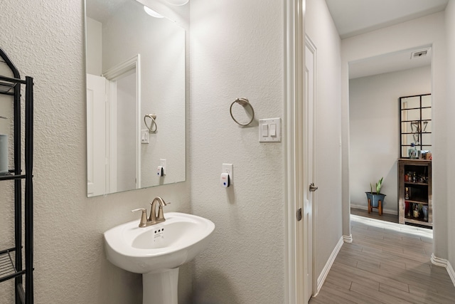 bathroom featuring baseboards, visible vents, wood tiled floor, a sink, and a textured wall