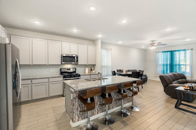 kitchen featuring a kitchen bar, a sink, open floor plan, appliances with stainless steel finishes, and wood tiled floor