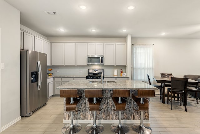 kitchen with visible vents, light stone countertops, a breakfast bar area, decorative backsplash, and appliances with stainless steel finishes