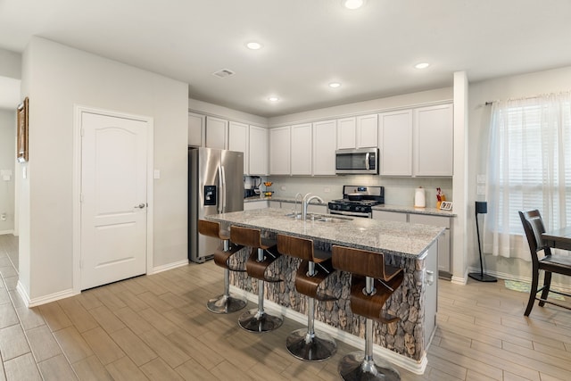 kitchen featuring light stone counters, a sink, light wood-style floors, appliances with stainless steel finishes, and a kitchen bar