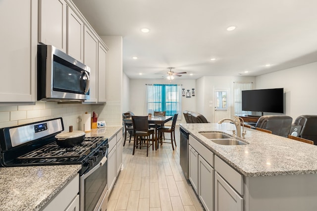 kitchen featuring tasteful backsplash, open floor plan, stainless steel appliances, a ceiling fan, and a sink