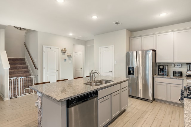 kitchen with wood finish floors, gray cabinetry, a sink, stainless steel appliances, and light stone countertops