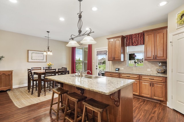586 Ruby Dr, Bellville, TX 77418 - kitchen featuring brown cabinetry, an island with sink, dark wood-type flooring, decorative light fixtures, and a sink