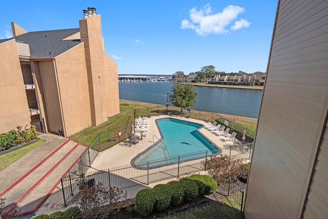 pool with a patio, a water view, and fence