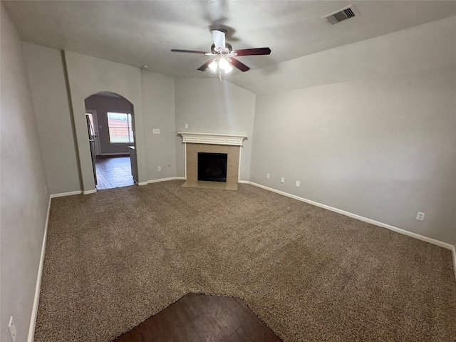 unfurnished living room featuring arched walkways, a fireplace, visible vents, dark carpet, and baseboards