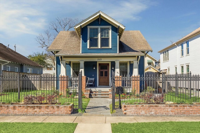 view of front facade with a fenced front yard, covered porch, roof with shingles, and a gate