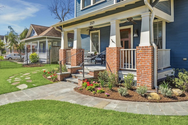 entrance to property featuring covered porch, fence, a ceiling fan, and brick siding