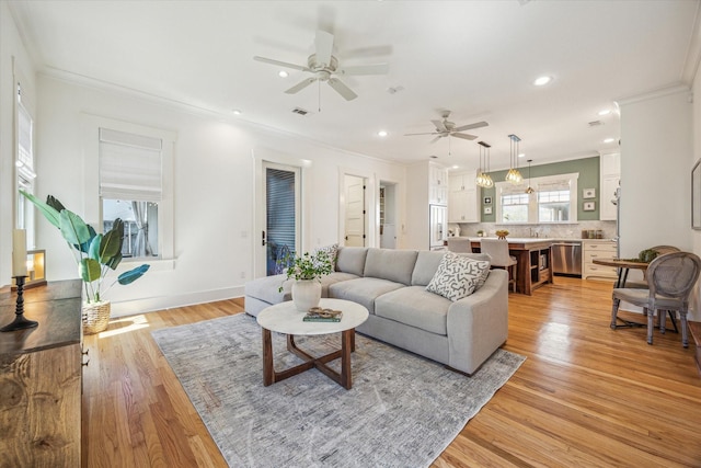 living area with ornamental molding, recessed lighting, light wood-style flooring, and a healthy amount of sunlight