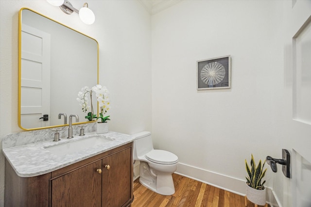 half bath with vanity, wood finished floors, toilet, and baseboards