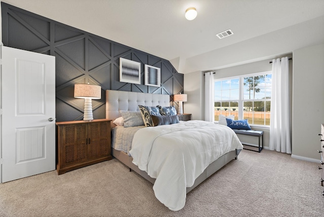 bedroom with visible vents, a decorative wall, light carpet, and baseboards