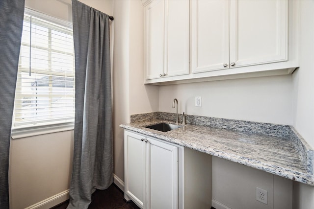 kitchen with baseboards, white cabinetry, light stone counters, and a sink