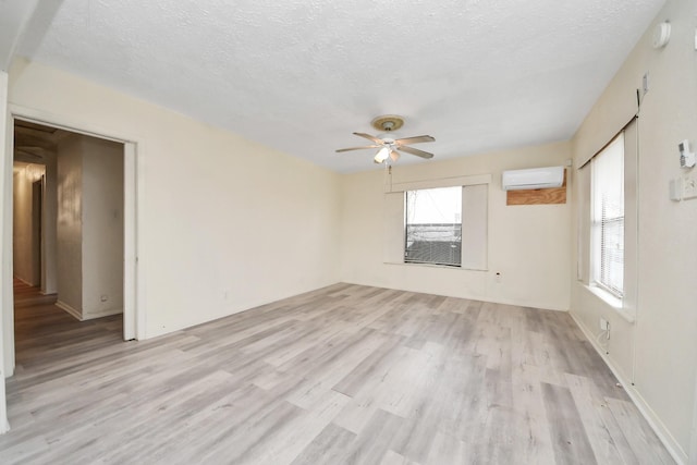 empty room featuring a textured ceiling, a wall mounted AC, light wood-style flooring, and a ceiling fan