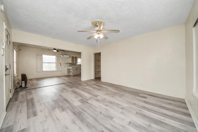 unfurnished living room with a wall unit AC, heating unit, light wood finished floors, ceiling fan, and a textured ceiling