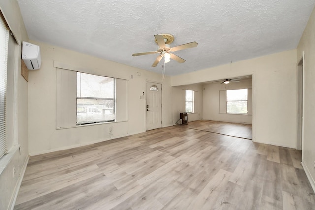 interior space featuring a textured ceiling, a wall mounted air conditioner, light wood-style flooring, and a ceiling fan