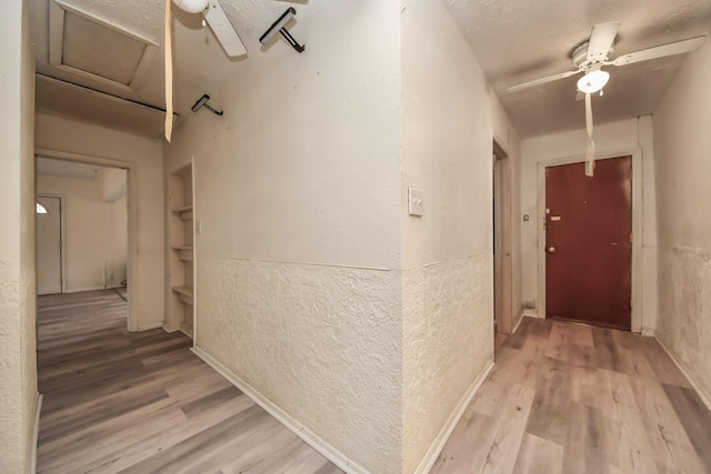 hall featuring light wood-type flooring, built in shelves, a textured ceiling, and a textured wall