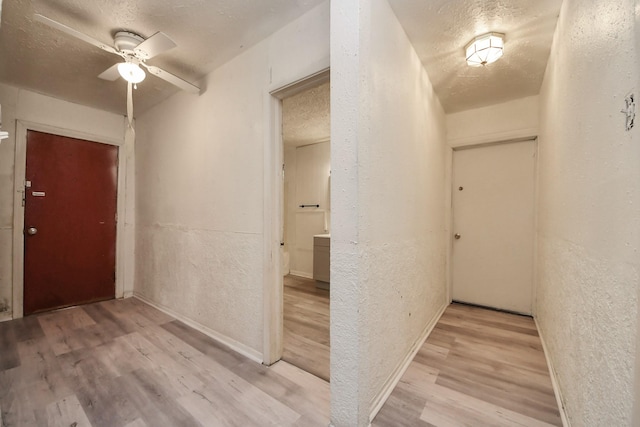 corridor with light wood finished floors, baseboards, a textured ceiling, and a textured wall