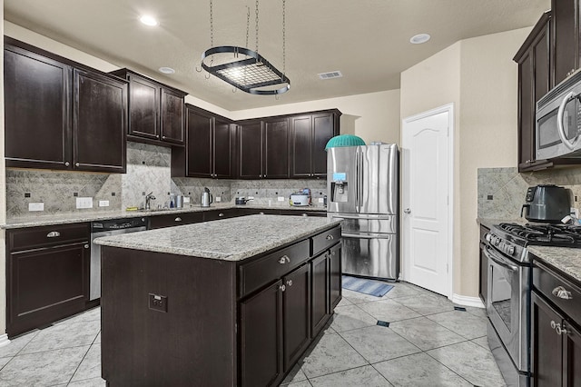 kitchen featuring a center island, visible vents, appliances with stainless steel finishes, dark brown cabinetry, and light stone countertops