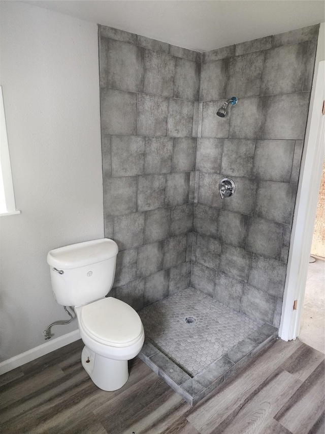 bathroom with a tile shower, wood finished floors, toilet, and baseboards