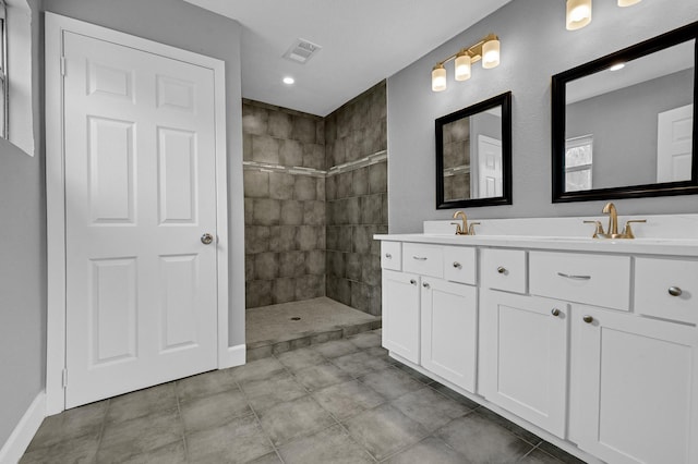 full bath featuring double vanity, visible vents, a sink, and tiled shower