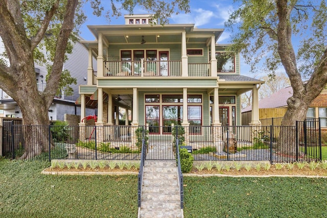 view of front facade featuring fence private yard, ceiling fan, a balcony, and a front lawn