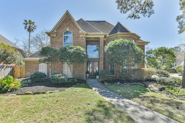 view of front of home featuring brick siding, fence, a front lawn, and french doors