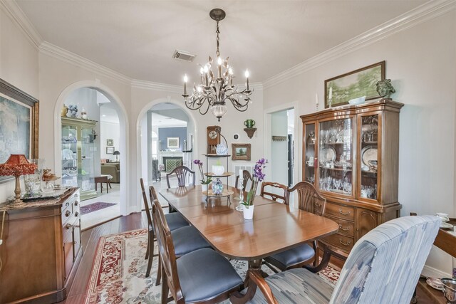 dining space with visible vents, arched walkways, dark wood-style floors, ornamental molding, and a notable chandelier